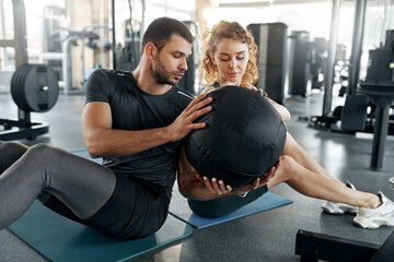 Fit man and woman doing partner workout using a medicine ball during core training session in gym....