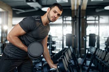 Close-up of athletic man exercising with dumbbell in gym. Focus on muscular arm and intense...