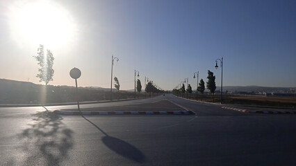 A wide-angle landscape shot of a deserted road during late afternoon or early evening, with the sun...