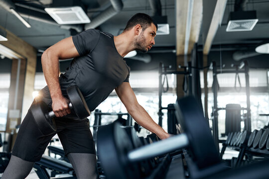Young athletic man performing biceps curls with dumbbells in a modern gym. Strength and determination. Concept: fitness, workout, motivation.