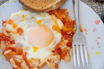 un huevo estrellado sobre salsa de jitomate con pan tostado y tenedor
