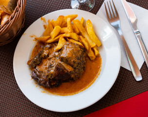 Stewed pork in broth with fried potato served in a plate with other table appointments