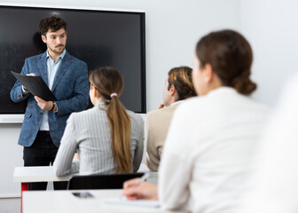Male business coach standing near interactive board explaining topic while standing against group...