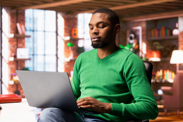 Man enjoying watching TV show on notebook during relaxation time at home. African american person...