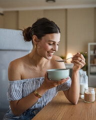 Portrait of woman sit at table in the living room and eat oatmeal