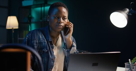 Woman receiving phone call from friend while working from home on laptop in personal office....