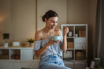 Portrait of woman sit on sofa in the living room and eat oatmeal
