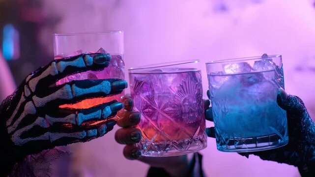 Skeleton hand holding glowing purple and blue cocktails, ready for a Halloween toast.
