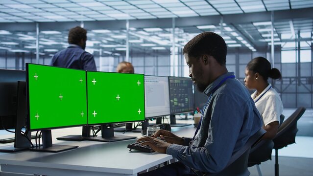Technician using multi monitor green screen computer setup, working in server farm to optimize it for data processing requirements. Man doing developing on chroma key PC in data center