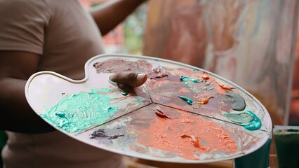 In an art studio, painter mixes multiple watercolor paints on a palette to create artwork on...