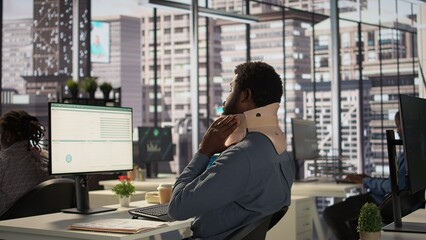 Hurt employee with a cervical collar working on a new business project, struggling to sit at the...