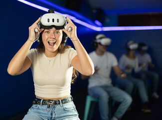 Portrait of a emotional girl actively playing a virtual video game in a VR helmet using joysticks...