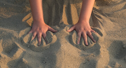 children's hands playing in beach sand