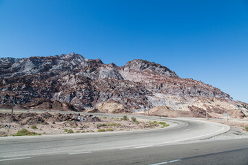 Colorful layered mountains along a coastal road in Hormozgan, Iran. A stunning display of geological patterns under a clear blue sky, perfect for nature and travel themes