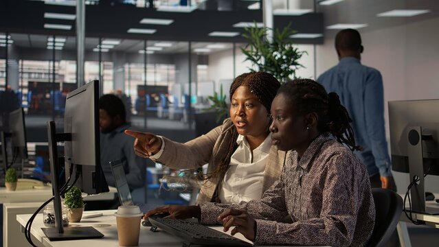 African american businesswomen collaborating on monthly revenue balance calculation, strategizing a plan for enterprise development. Team of executive staff evaluating analytics on pc. Camera B.