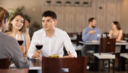 Three friends meeting in modern restaurant - men and a woman drinking wine, talking, discussing problems
