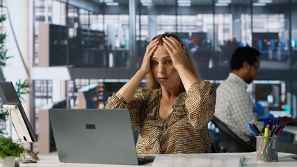Stressed businesswoman in corporate attire experiences a migraine as she juggles multiple business...