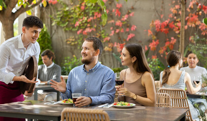 Waiter takes an order from a couple in love who decided to meet in an open-air restaurant