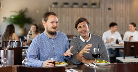 Couple young and adult man eating drinking and talking in restaurant