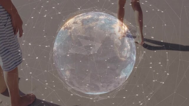 Brother and sister shifting on beach as pulsing digital globe hovers, showcasing tech network