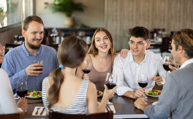 Group of men and women friends eating drinking and talking in restaurant