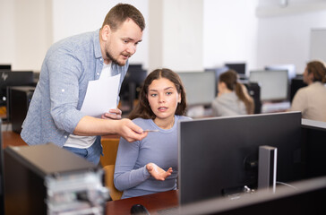 Man teacher helps girl with learning on computer in university computer class