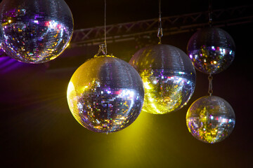 Escena con 5 bolas de espejos suspendidas bajo luces cálidas amarillas, evocando la atmósfera de una fiesta en club nocturno.