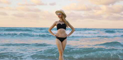Summer vacation, beautiful young woman in swimsuit, hat standing on sea beach background