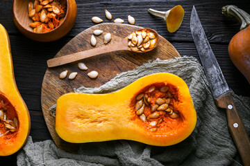Flat lay of raw butternut squash with rustic cutlery and scattered seeds on wooden background. Cozy fall still life for food prep or autumn kitchen inspiration