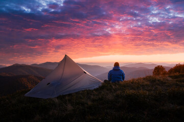 Autumn mountains glow under vibrant sunset as hiker rests near his tent. Peaceful fall scenery...