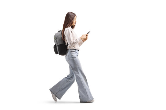  Full length profile shot of a female teenager walking and looking at a mobile phone