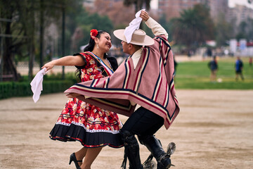 Portrait of a smiling young couple dressed as Chilean huasos, posing and joyfully dancing cueca...