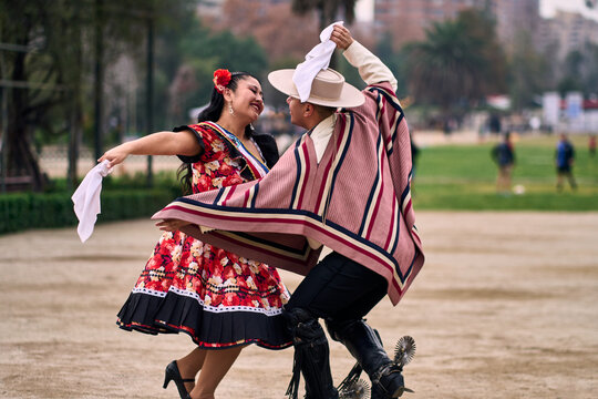 Portrait of a smiling young couple dressed as Chilean huasos, posing and joyfully dancing cueca outdoors. Traditional Chilean dance. Chilean traditions, celebrations, and culture.