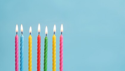 Row of colorful birthday candles burning brightly. Twirled wax sticks in pink, blue, yellow, red, and green stand against a soft blue background, creating a festive atmosphere of celebration and joy.