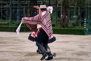 Fototapeta premium Portrait of a smiling young couple dressed as Chilean huasos, posing and joyfully dancing cueca outdoors. Traditional Chilean dance. Chilean traditions, celebrations, and culture.