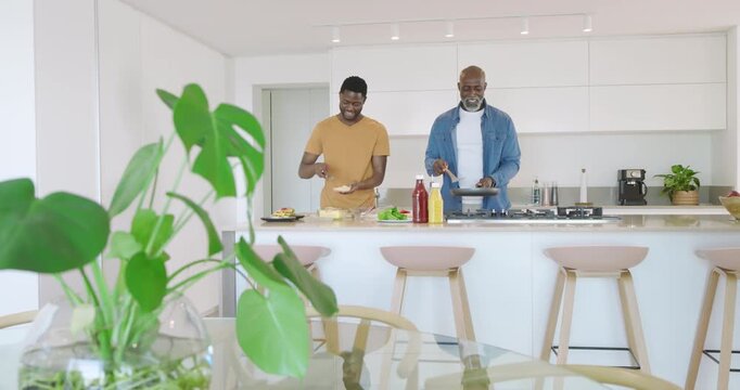 African American dad and son slicing loaf flipping pancakes assembling plates at bar for breakfast
