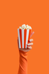 Womans hand holding striped box with popcorn on an orange background