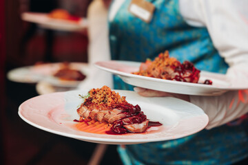 Waiter in uniform serving dishes on party event, server carrying plates with food at the table,...