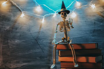 Halloween Stories.Skeleton Toy Sitting on Book with Lights. Book, skeleton and glowing garland in...