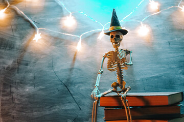 Skeleton Wearing Witch Hat on Stack of Books. Skeleton sitting on book and garlands in blue green...