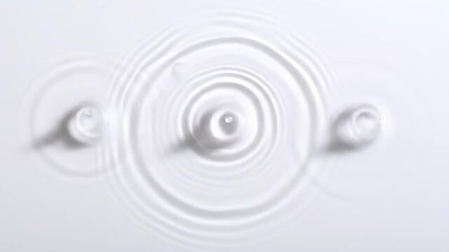 Aerial view of clear liquid with three ripples of water created by drops. The circular waves expand outwards. Minimalist composition