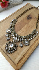 Sparkling necklace with clear gemstones and gold accents rests elegantly on a light wood surface, showcasing craftsmanship and a vintage-inspired jewelry design for fashion and accessory collections.