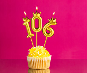 Yellow birthday cupcake with a number 106 candle - Birthday card on a pink background