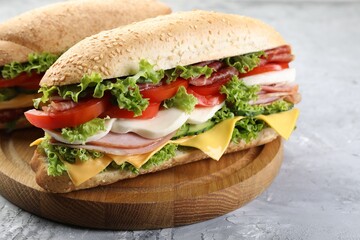 Tasty baguette sandwiches with ham, cheese and vegetables on grey textured table, closeup