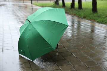 Green umbrella on wet asphalt under heavy rain, space for text