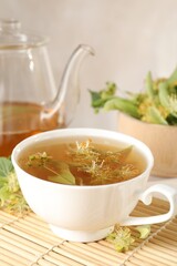 Fresh linden tea in cup, teapot and flowers on table, closeup