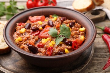 Tasty chili con carne in bowl on wooden table, closeup