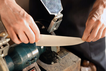 Man sharpening knife with bench grinder indoors, closeup