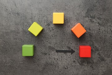 Maximum. Colorful cubes and arrow pointing at red one on grey table, flat lay