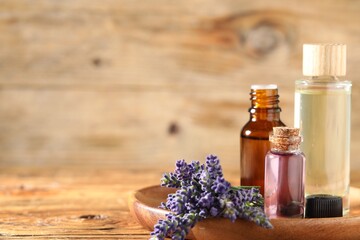 Bottles of lavender essential oil and flowers on wooden table, closeup. Space for text